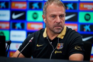 Hansi Flick en rueda de prensa antes del derbi, luciendo una camiseta oficial del club.